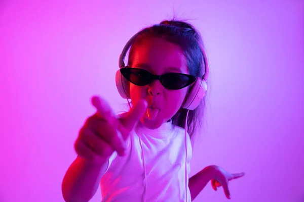 Porträt eines kleinen Mädchens mit Kopfhörern auf lila Gradienten Hintergrund in Neonlicht — Stockfoto