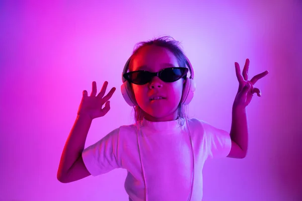 霓虹灯中紫色渐变背景的耳机中小女孩的肖像 — 图库照片