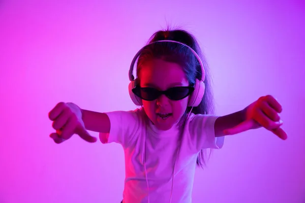 Portret van klein meisje in koptelefoon op paarse gradiënt achtergrond in neon licht — Stockfoto