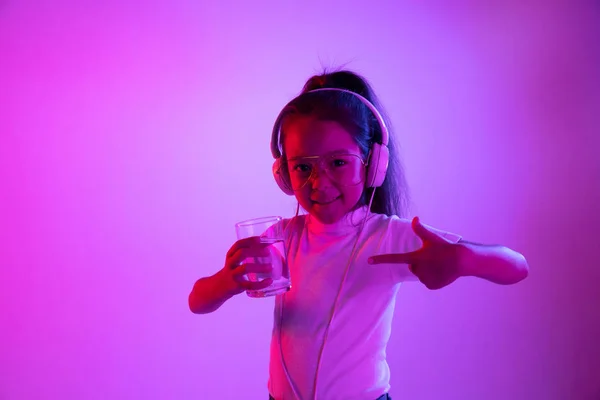 Porträtt av liten flicka i hörlurar på lila gradient bakgrund i neonljus — Stockfoto
