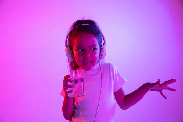 Portrait de petite fille en casque sur fond dégradé violet au néon — Photo