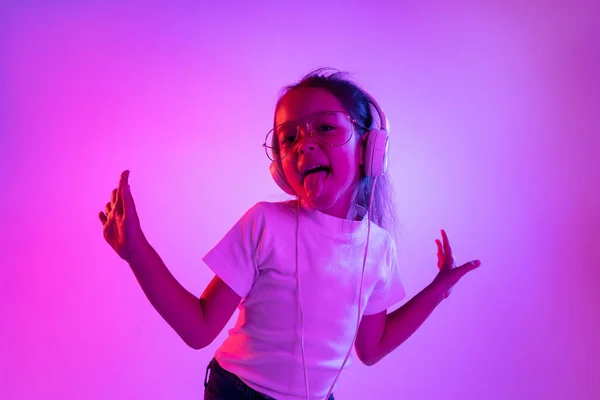 Portrait de petite fille en casque sur fond dégradé violet au néon — Photo