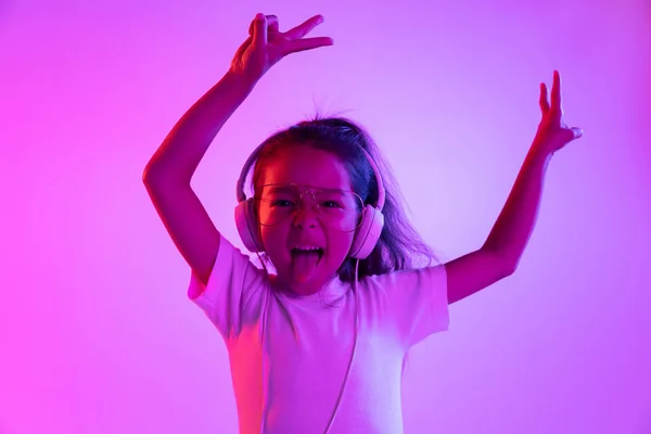 Portrait de petite fille en casque sur fond dégradé violet au néon — Photo