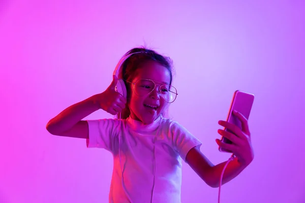 Портрет маленькой девочки в наушниках на фиолетовом градиентном фоне в неоновом свете — стоковое фото