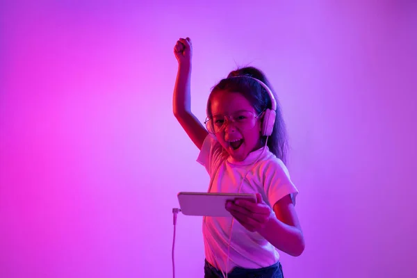 Portrait de petite fille en casque sur fond dégradé violet au néon — Photo