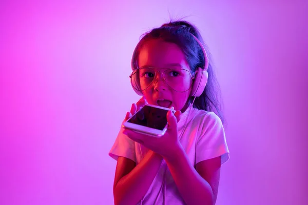 ネオン光の紫色のグラデーションの背景にヘッドフォンで小さな女の子の肖像画 — ストック写真
