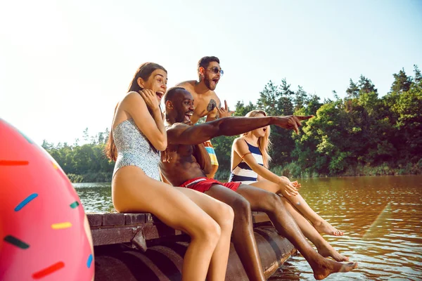 Group of happy friends having fun while sitting and laughting on the pier on river — Stock Photo, Image