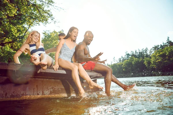 강에 부두에 앉아서 웃으면서 즐거운 시간을 보내는 행복한 친구들 — 스톡 사진