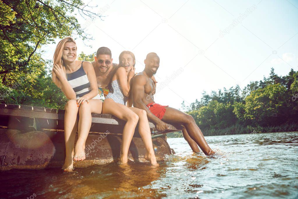 Group of happy friends having fun while sitting and laughting on the pier on river