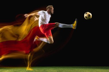 Erkek futbolcu karışık ışıkta koyu arka planda topa tekme