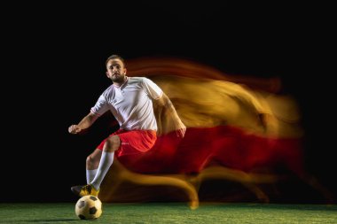 Erkek futbolcu karışık ışıkta koyu arka planda topa tekme