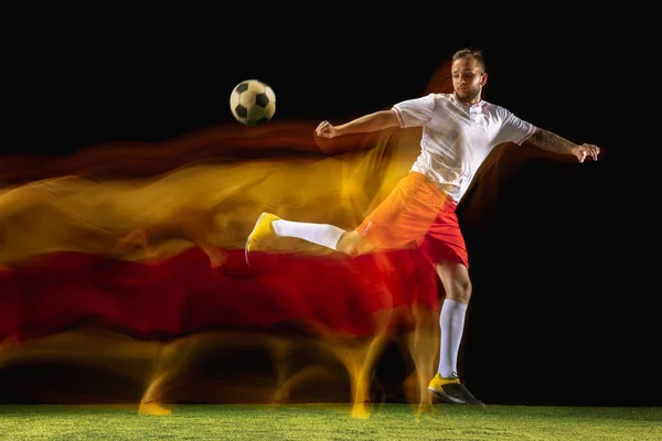 Mannelijke voetbalspeler schoppen bal op donkere achtergrond in gemengd licht — Stockfoto