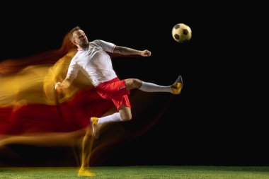 Erkek futbolcu karışık ışıkta koyu arka planda topa tekme