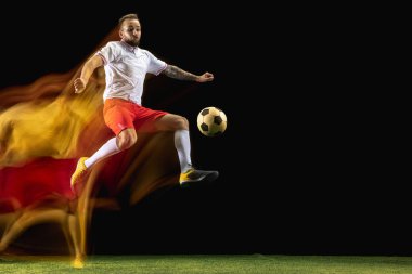 Erkek futbolcu karışık ışıkta koyu arka planda topa tekme