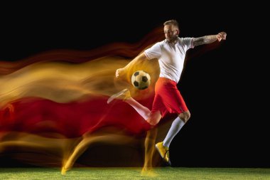Erkek futbolcu karışık ışıkta koyu arka planda topa tekme