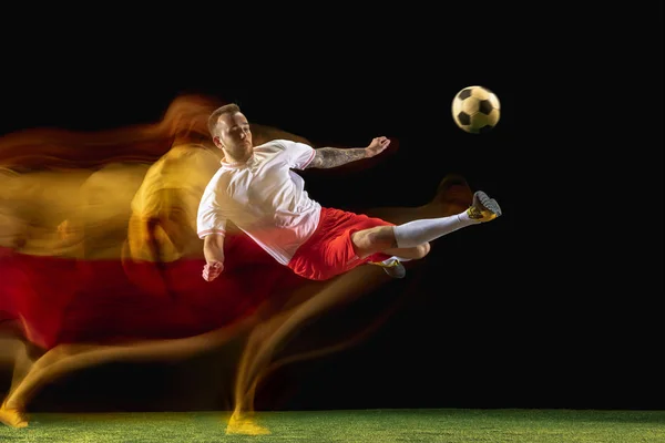 Férfi focista rúgás labdát a sötét háttér vegyes fényben — Stock Fotó