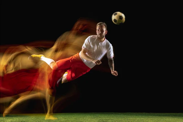 Mannelijke voetbalspeler schoppen bal op donkere achtergrond in gemengd licht — Stockfoto