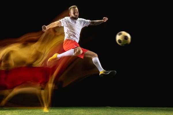 Jogador de futebol masculino chutando bola no fundo escuro em luz mista — Fotografia de Stock