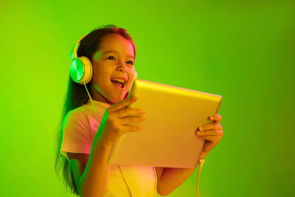 Portret małej dziewczynki w słuchawkach na zielonym tle w świetle neonowym — Zdjęcie stockowe