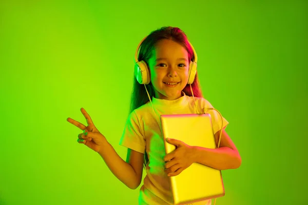 Portret małej dziewczynki w słuchawkach na zielonym tle w świetle neonowym — Zdjęcie stockowe