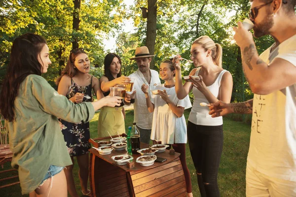 Amigos felizes comendo e bebendo cervejas no jantar de churrasco na hora do pôr do sol — Fotografia de Stock