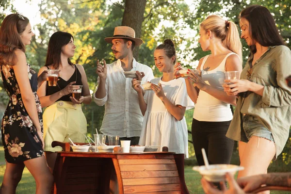 Amigos felices comiendo y bebiendo cervezas en la cena de barbacoa al atardecer —  Fotos de Stock