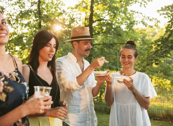 Amigos felices comiendo y bebiendo cervezas en la cena de barbacoa al atardecer —  Fotos de Stock