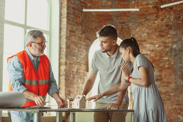 Foreman or achitect shows house, office or store design plans to a young couple