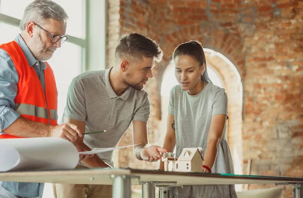 Foreman or achitect shows house, office or store design plans to a young couple