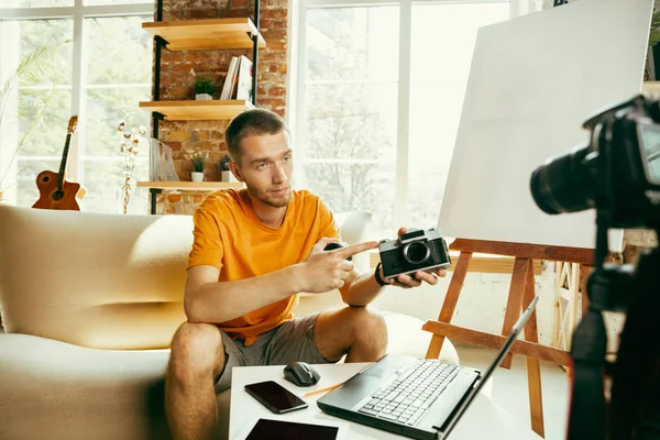 Caucasian male blogger with camera recording video review of gadgets at home