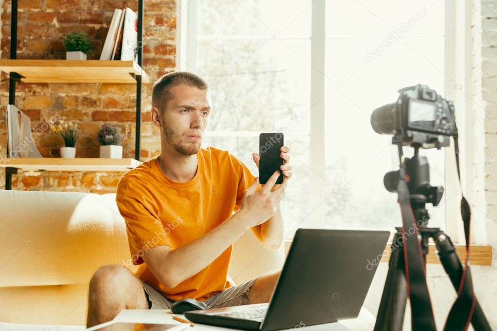 Caucasian male blogger with camera recording video review of gadgets at home