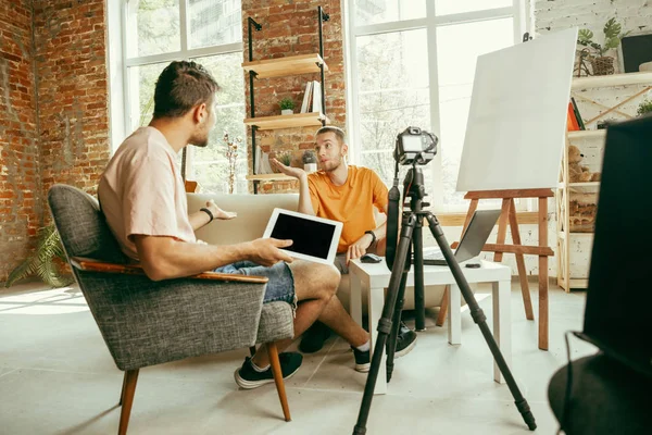 Two young male bloggers with professional camera recording video interview at home