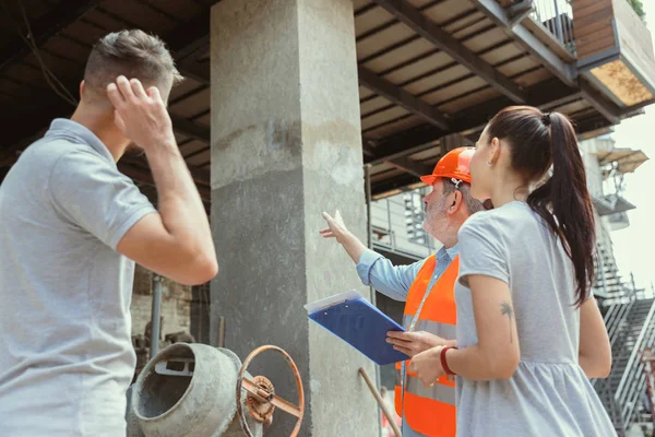 Polier oder Architekt zeigt jungen Paaren Pläne für Haus, Büro oder Geschäft — Stockfoto