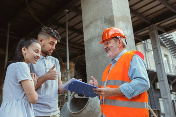 Polier oder Architekt zeigt jungen Paaren Pläne für Haus, Büro oder Geschäft — Stockfoto