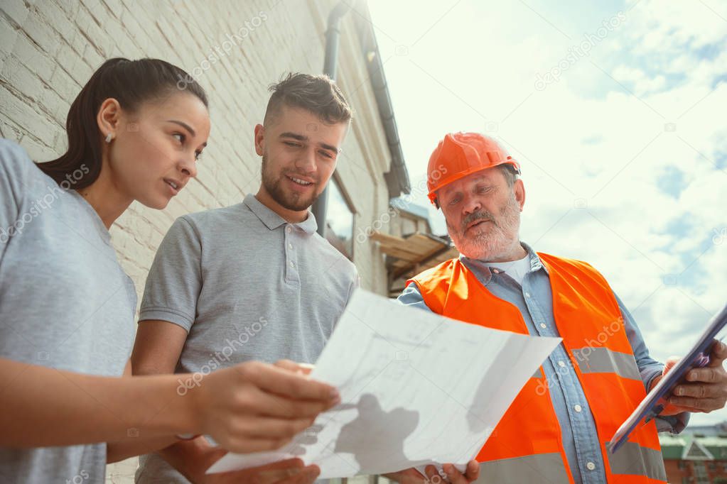 Foreman or achitect shows house, office or store design plans to a young couple