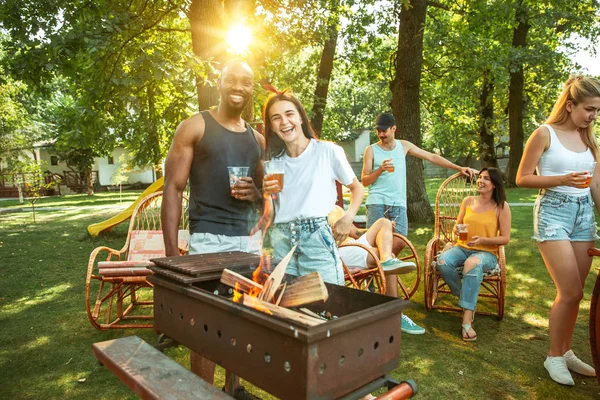 Amigos felizes estão tomando cerveja e churrasco no dia ensolarado — Fotografia de Stock