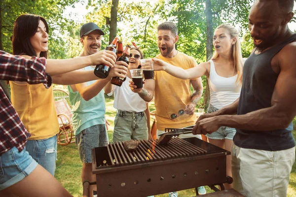 Amigos felizes estão tomando cerveja e churrasco no dia ensolarado — Fotografia de Stock