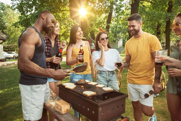 Amigos felizes estão tomando cerveja e churrasco no dia ensolarado — Fotografia de Stock