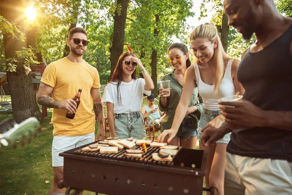 Amigos felizes estão tomando cerveja e churrasco no dia ensolarado — Fotografia de Stock