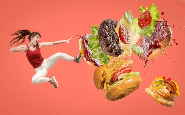 Fast Food-Konzept. junge Frau kämpft mit Burger auf rotem Hintergrund — Stockfoto