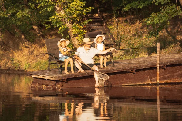 Χαριτωμένα κοριτσάκια και ο παππούς τους είναι στο ψάρεμα στη λίμνη ή το ποτάμι — Φωτογραφία Αρχείου