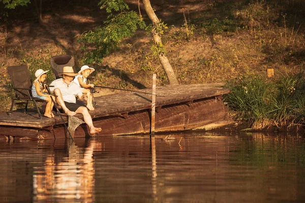Roztomilá děvčátka a jejich děda loví u jezera nebo řeky — Stock fotografie