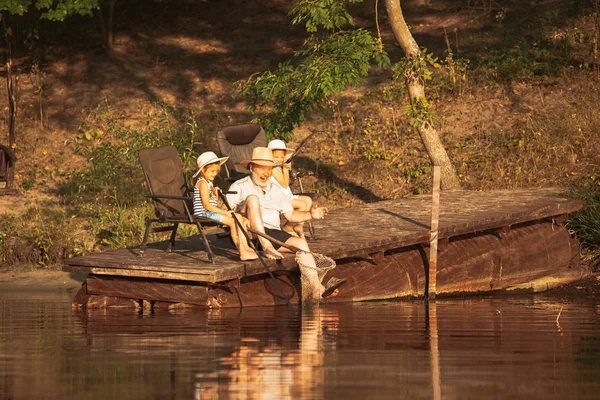 Roztomilá děvčátka a jejich děda loví u jezera nebo řeky — Stock fotografie