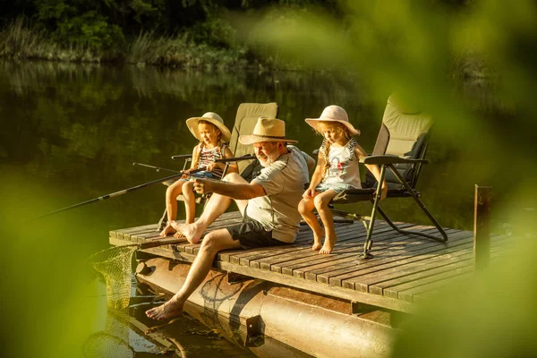 Χαριτωμένα κοριτσάκια και ο παππούς τους είναι στο ψάρεμα στη λίμνη ή το ποτάμι — Φωτογραφία Αρχείου