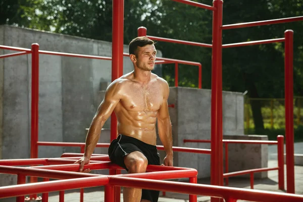 Joven hombre musculoso mientras hace su entrenamiento fuera en el patio de recreo — Foto de Stock