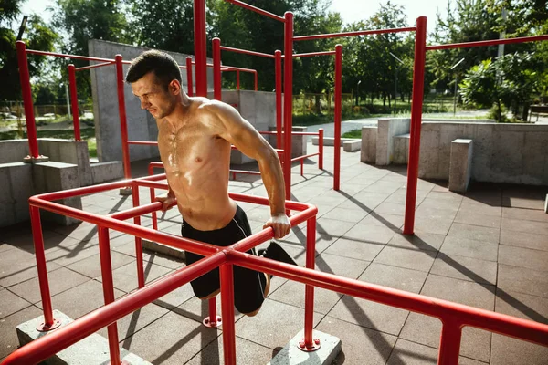 Joven hombre musculoso mientras hace su entrenamiento fuera en el patio de recreo —  Fotos de Stock