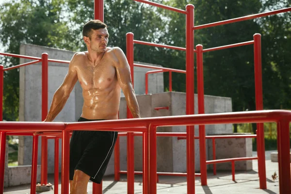 Joven hombre musculoso mientras hace su entrenamiento fuera en el patio de recreo —  Fotos de Stock