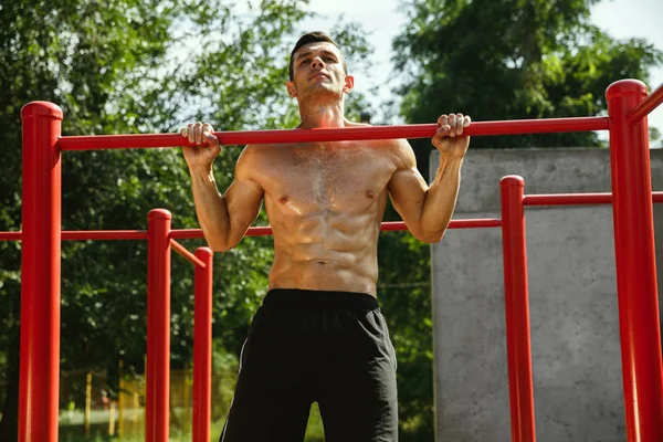 Young muscular man while doing his workout outside at playground