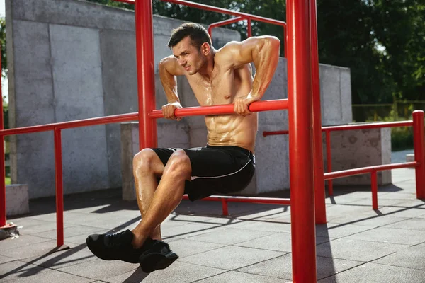 Joven hombre musculoso mientras hace su entrenamiento fuera en el patio de recreo — Foto de Stock