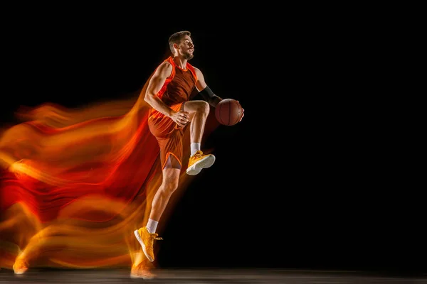 Jovem jogador de basquete caucasiano contra fundo escuro em luz mista — Fotografia de Stock